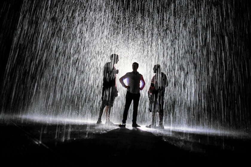Random International's Tom Stacey, left, Hannes Koch and Dev Joshi drink their coffee and converse while standing inside the newly assembled Rain Room, which will be on exhibit at LACMA in Los Angeles on Oct. 26, 2015.