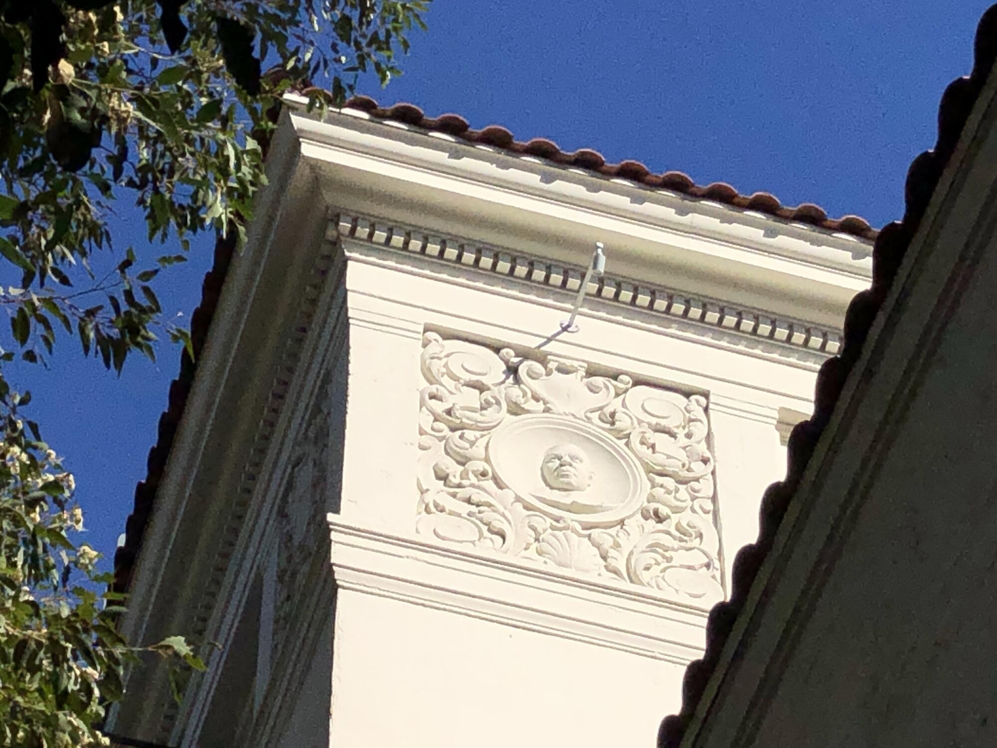 The corner of a building's ornate roofline, featuring a bas relief of a man and Spanish roof tile.