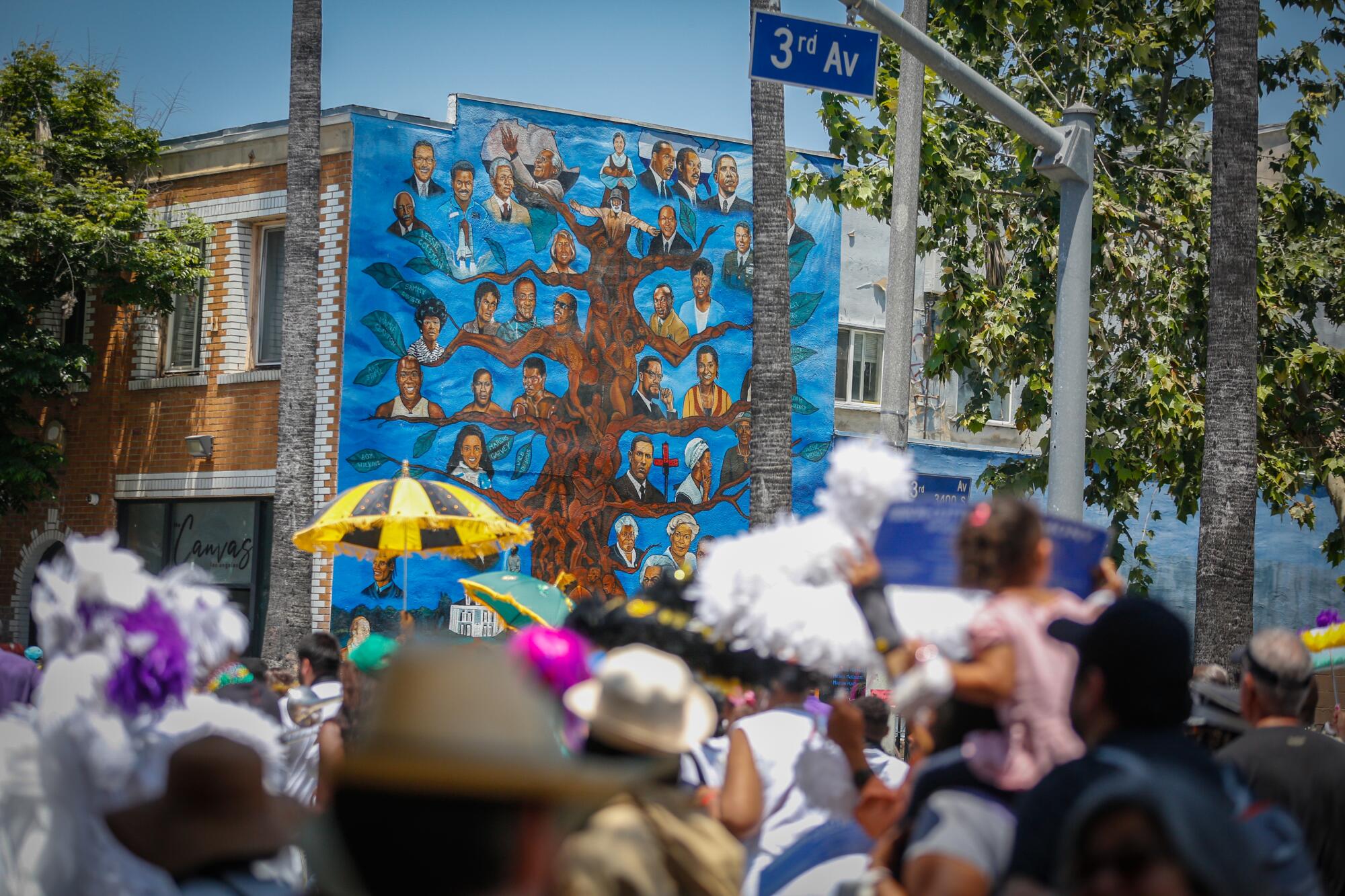 Community members celebrating the newly named, "New Orleans Corridor" pass a A mural of Black leaders in Los Angeles.