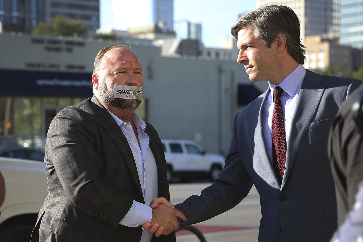 FILE - Alex Jones, left, arrives at the Travis County Courthouse in Austin, Texas, on July 26, 2022, with a piece of tape over his mouth that reads "Save the 1st." He shook hands with his lawyer, Andino Reynal. Although Jones portrays the lawsuit against him as an assault on the First Amendment, the parents who sued him say his statements were so malicious and obviously false that they fell well outside the bounds of speech protected by the constitutional clause. (Briana Sanchez/Austin American-Statesman via AP, Pool, File)