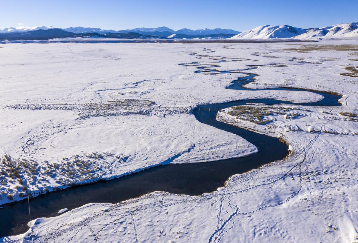 Aerial view of a winding river in a snow-covered valley with mountains in the background