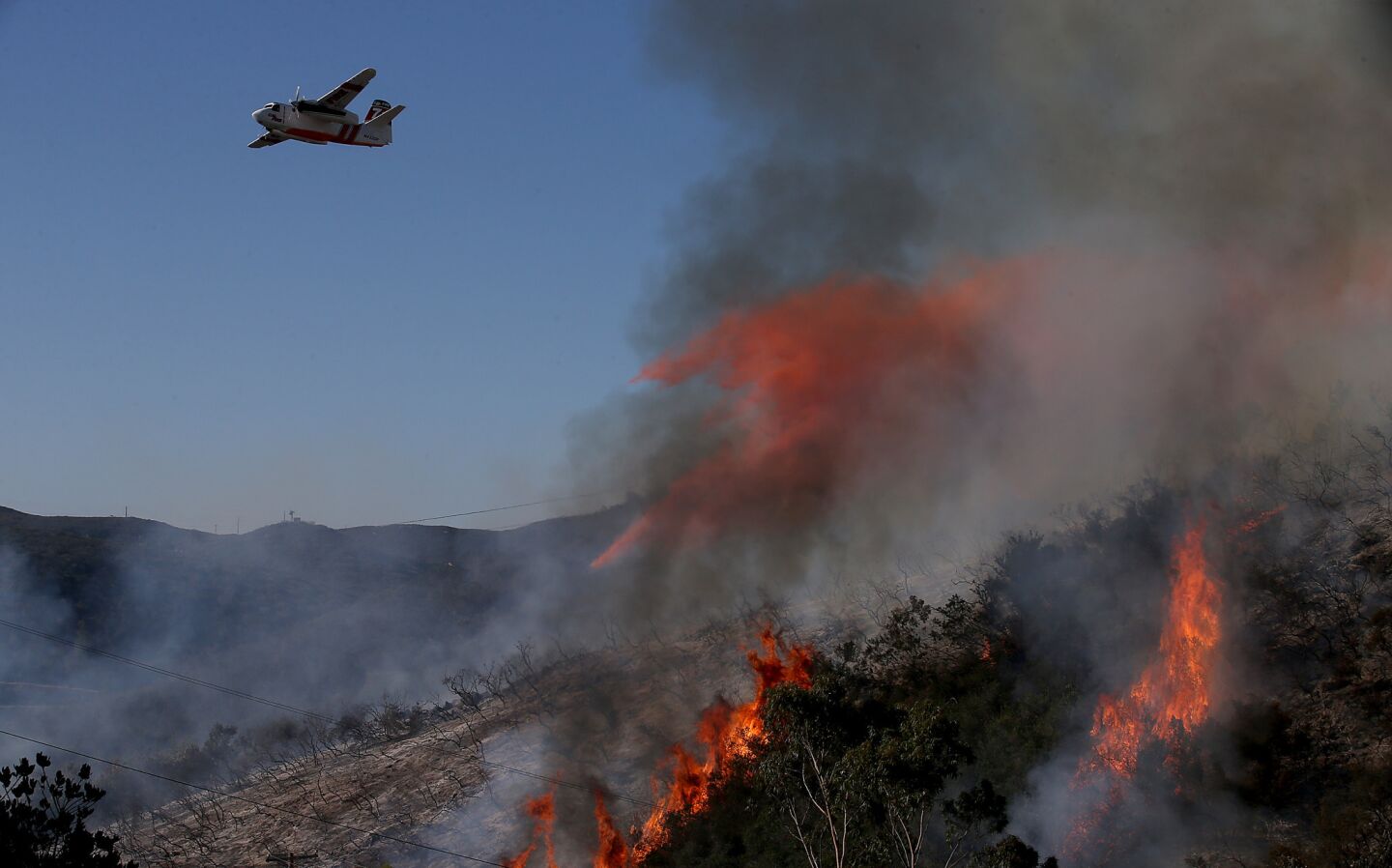 A firefighting airplane drops fire retardant on burning brush along Crestwind Spur Road in San Marcos.