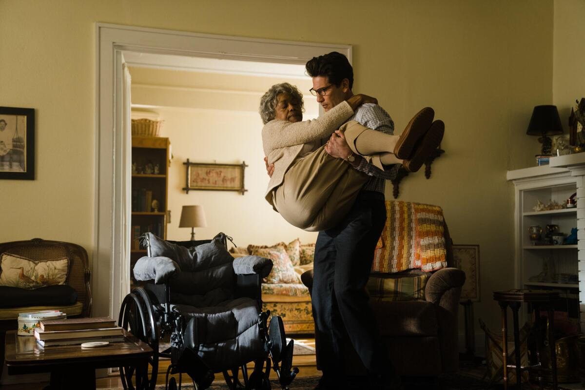 An elderly woman is carried by a younger man in a living room.