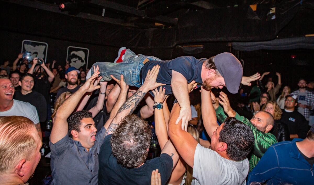A person is held up by audience members as he crowd surfs during a comedy performance.