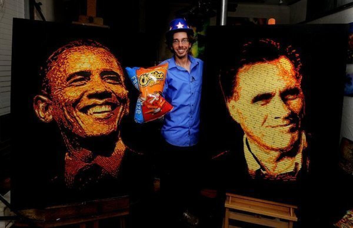Artist Jason Baalman poses in front of portraits of President Obama and GOP challenger Mitt Romney that were made entirely of more than 2,000 individual Cheetos snacks.
