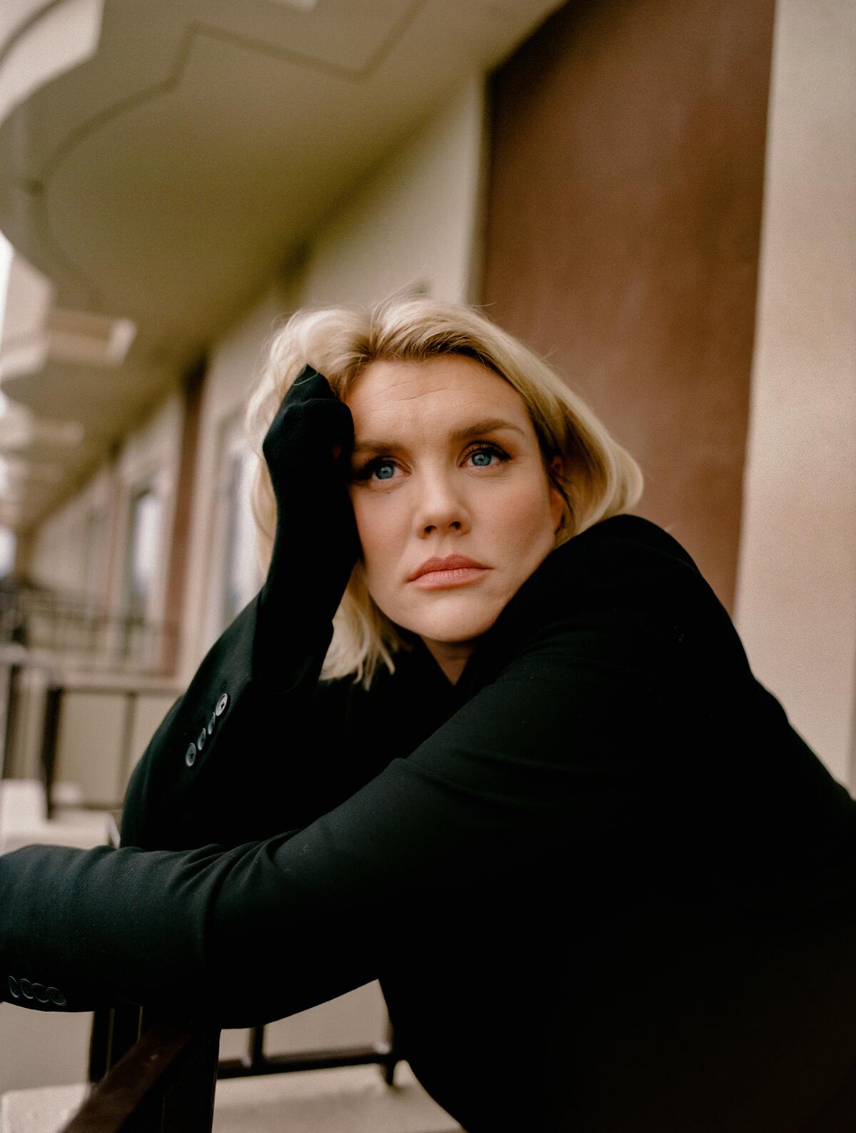 Emerald Fennell wears a black sweater and leans her head on her hand for a portrait.