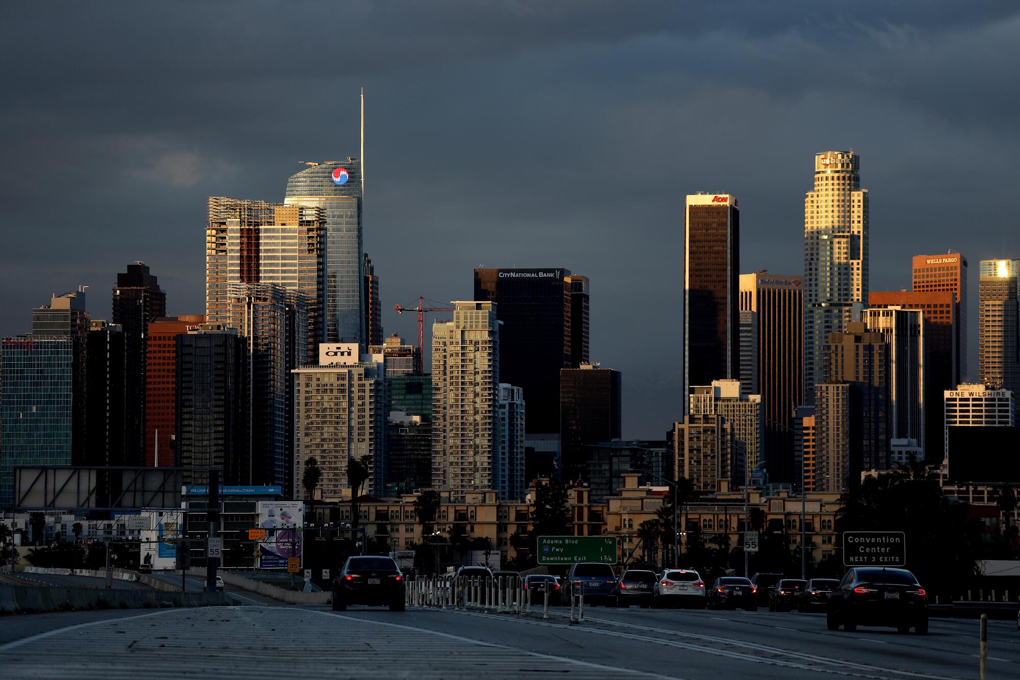 Clouds hover in the background of a condensed view of downtown Los Angeles skyline partially lit by a sunset.