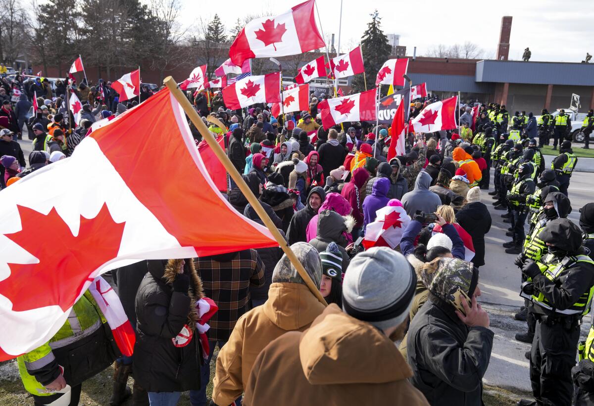Police officers hold a line as protesters wave Canadian flags 