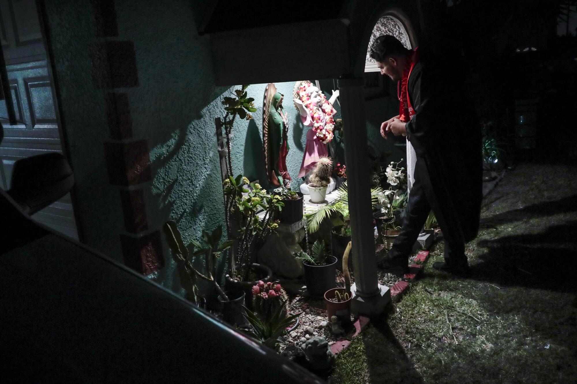 Cesar Martinez hangs his graduation lei on a Jesus statue outside his home 