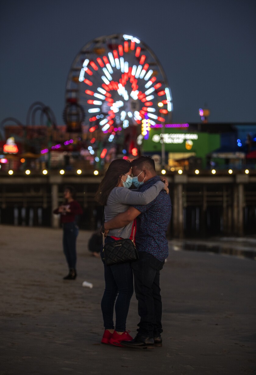 Both masked, Diana Mazariegos and her husband, Jonathan Gomez, of Riverside, embrace at dusk by the Santa Monica Pier.