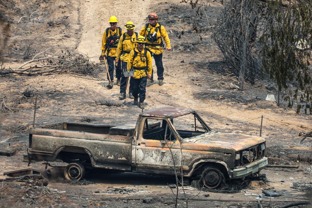 Firefighters walk toward a burned out truck.