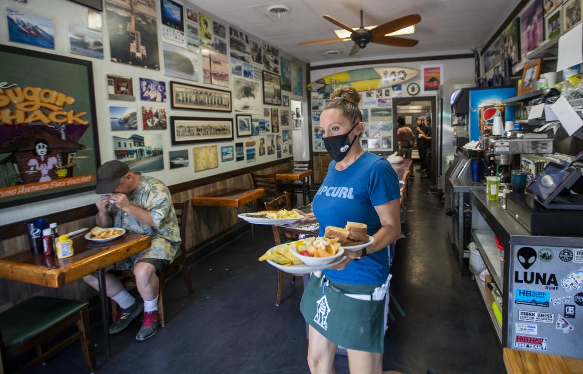 A waitress in a mask carries several plates of food