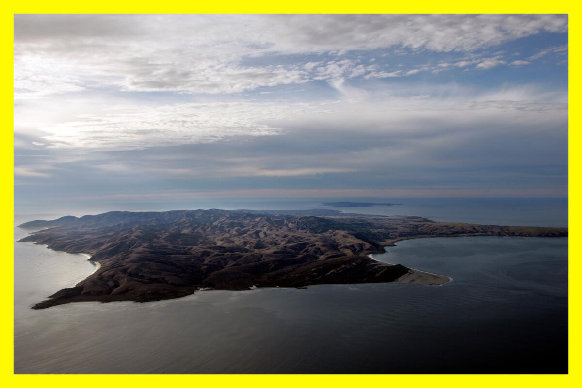 Aerial view of Santa Rosa Island surrounded by water with the sun peeking through clouds behind