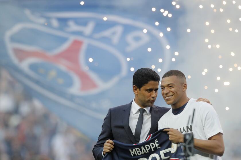 PSG President Nasser Al-Khelaifi, left, speaks to PSG's Kylian Mbappe who holds a shirt with his name and 2025 on it as it is announced he has signed a three year extension to his contract on the pitch ahead of the French League One soccer match between Paris Saint Germain and Metz at the Parc des Princes stadium in Paris, France, Saturday, May 21, 2022. (AP Photo/Michel Spingler)