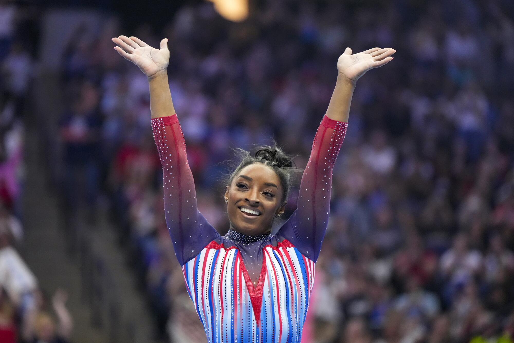Simone Biles smiles with her hands in the air.