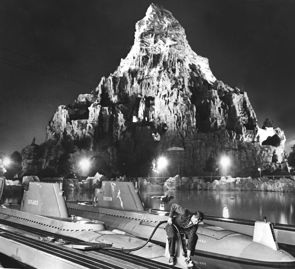 A person cleans a ride at Disneyland with the Matterhorn looming overhead in 1963