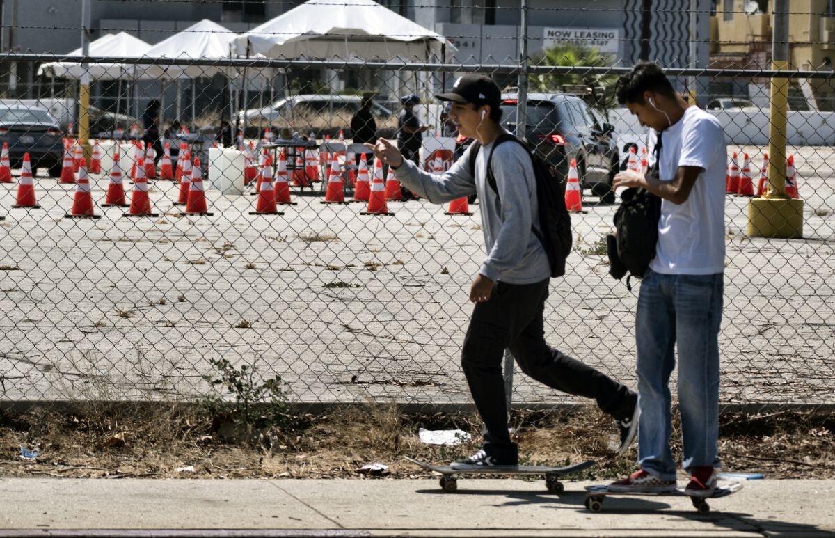 Skateboarders ride past a coronavirus testing site in the Panorama City section of Los Angeles on Tuesday, Aug. 3, 2020. A technical problem has caused a lag in California's tally of coronavirus test results, casting doubt on the accuracy of recent data showing improvements in the infection rate and hindering efforts to track the spread. (AP Photo/Richard Vogel)