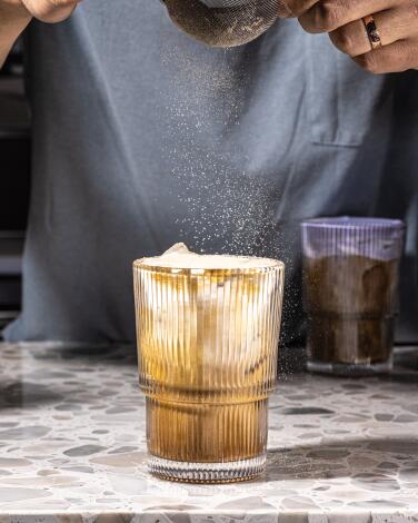 A barista sifts powder over a misugaru drink