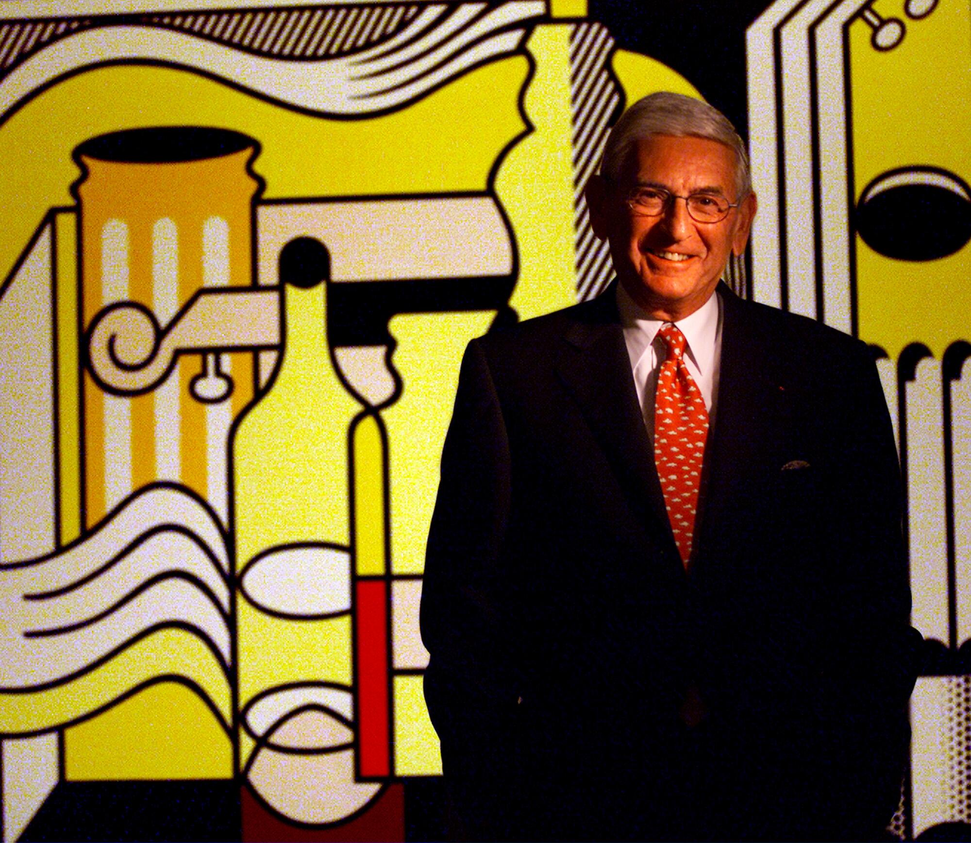 Eli Broad, in suit and tie, in front of a large, brightly colored painting.