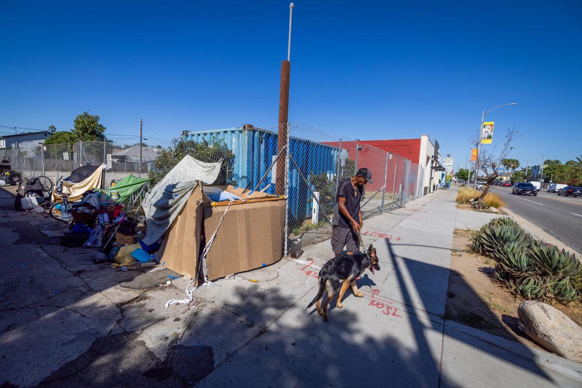 A man and his dog beside a sidewalk encampment