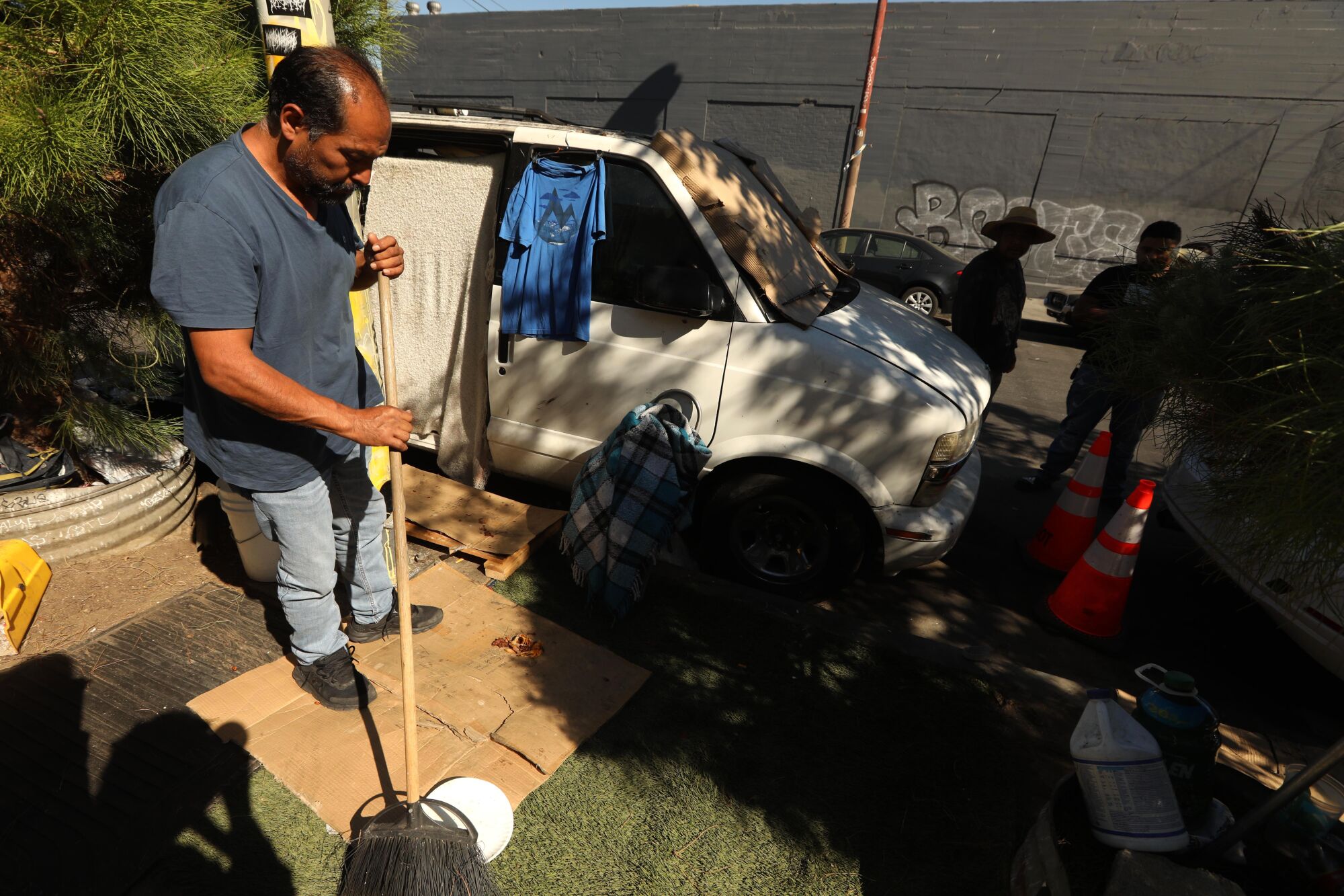 Miguel Meneses sweeps the area outside the van where he lives with his wife Sandra Torres in the Boyle Heights.