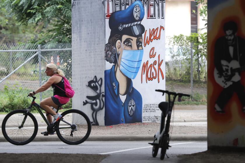 A bicyclist passes by a COVID-19 related wall painting in the Deep Ellum section of Dallas, Tuesday, June 30, 2020. (AP Photo/LM Otero)