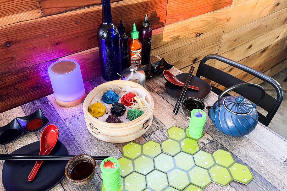 A table set with plates, a teapot, cups, spoons, chopsticks and rainbow-colored xiao long bao, as well as a board game