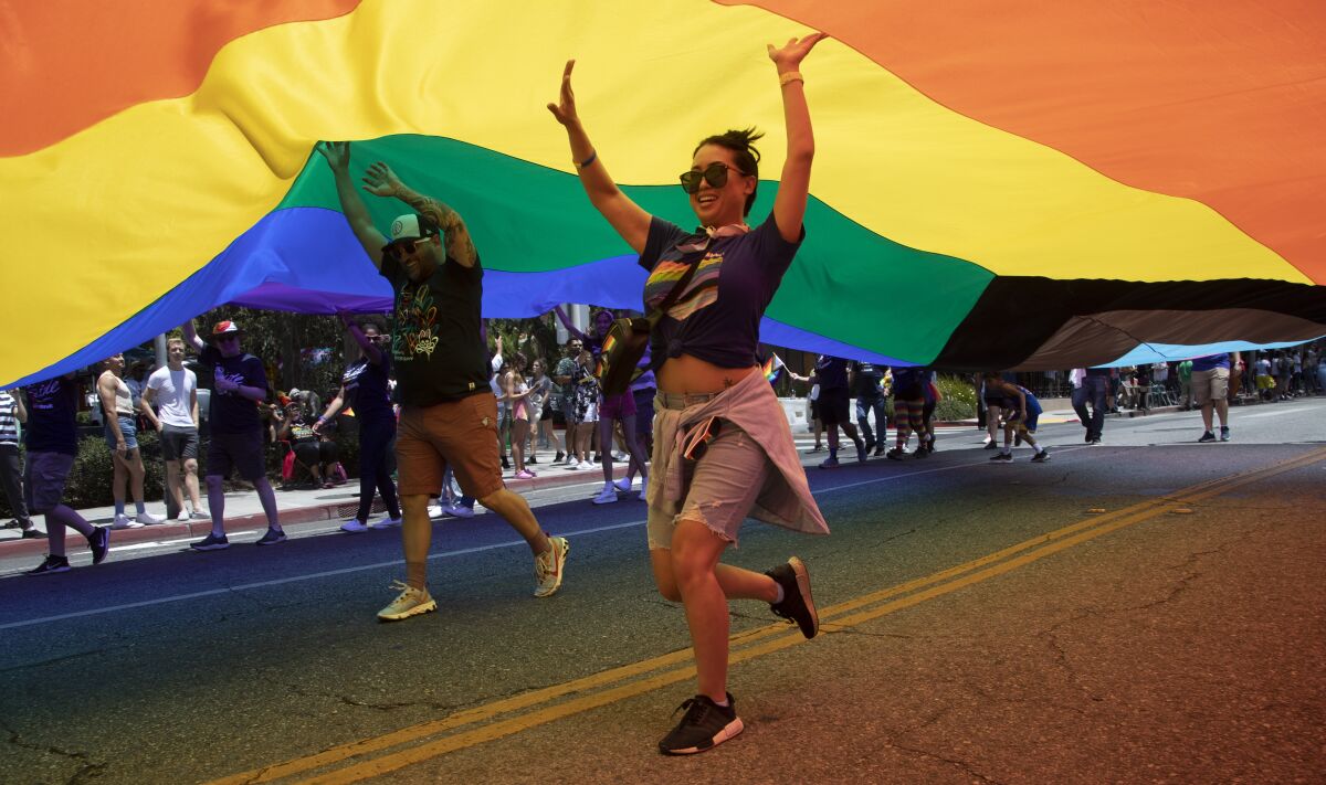 People run underneath a large rainbow flag