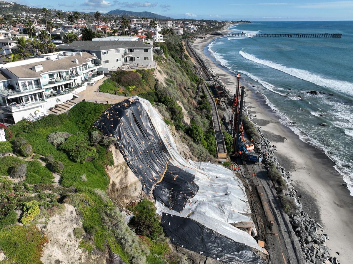 An aerial view of a landslide near cliff-top homes, protective tarping to prevent further slides from upcoming rain storms.