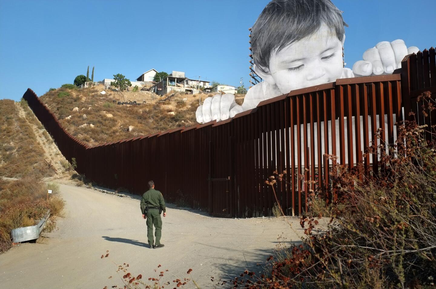 Un agente de la Patrulla Fronteriza estadounidense observa la obra 'Kikito', del artista y grafitero francés JR, en el muro que divide la frontera entre Tecate (Baja California, México) y San Diego (California, EEUU).