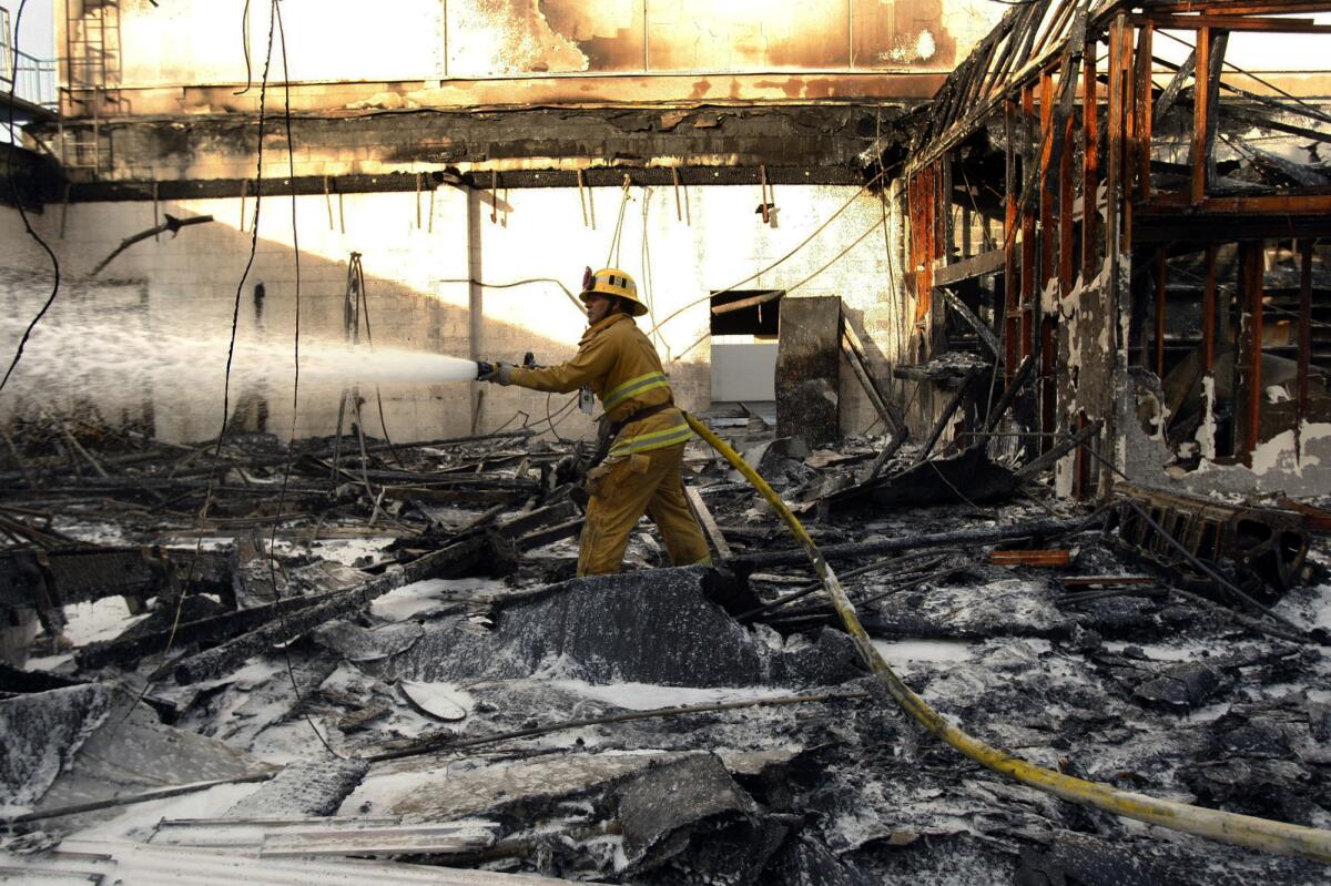 A firefighter aims water at the remains of a fire at a vacant car dealership that took just under three hours to knock down Monday.