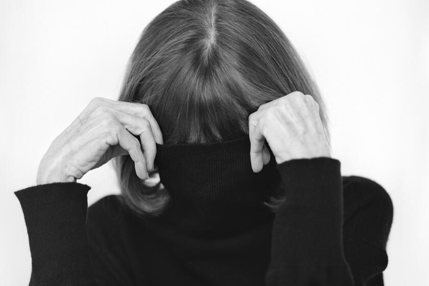 Joan Didion obscures her face behind a black turtle neck in black and white photographic portrait