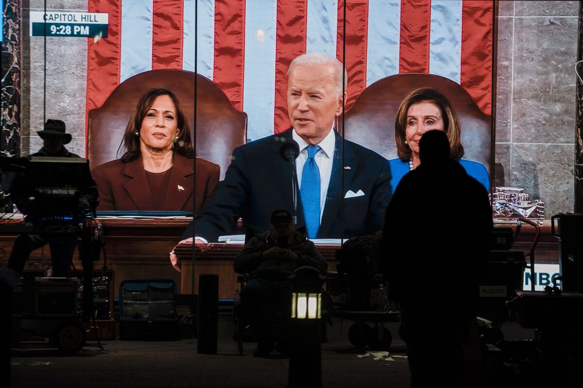 A TV news crew member sits in front of a live feed of President Joe Biden delivering his State of the Union address. 