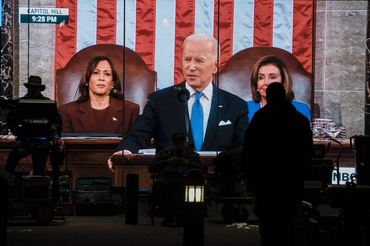 A TV news crew member sits in front of a live feed of President Joe Biden delivering his State of the Union address.
