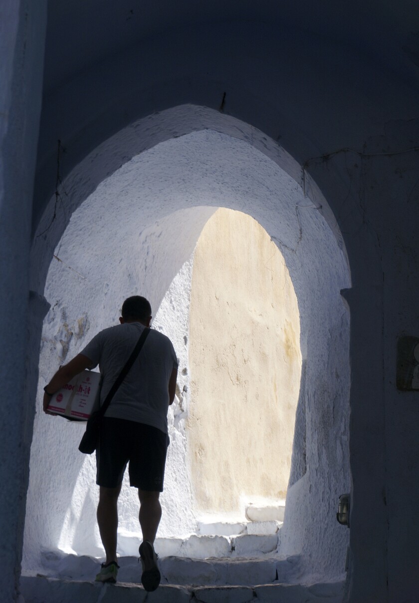 A man carries groceries down a steep alley in the compact, hilltop white village of Pyrgos on the island of Santorini, Greece.