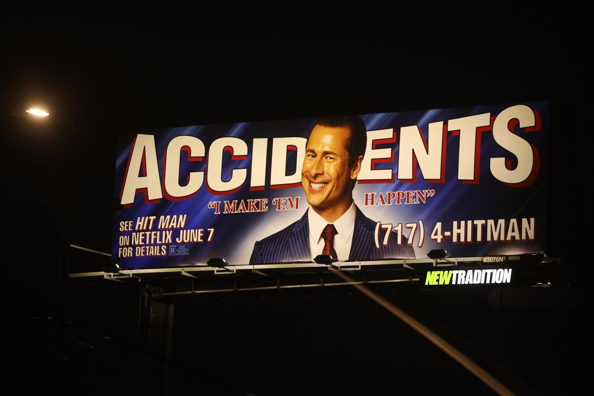 A billboard of a man smiling in front of the word Accidents is lighted up at night that advertises Netflix's "Hit Man."