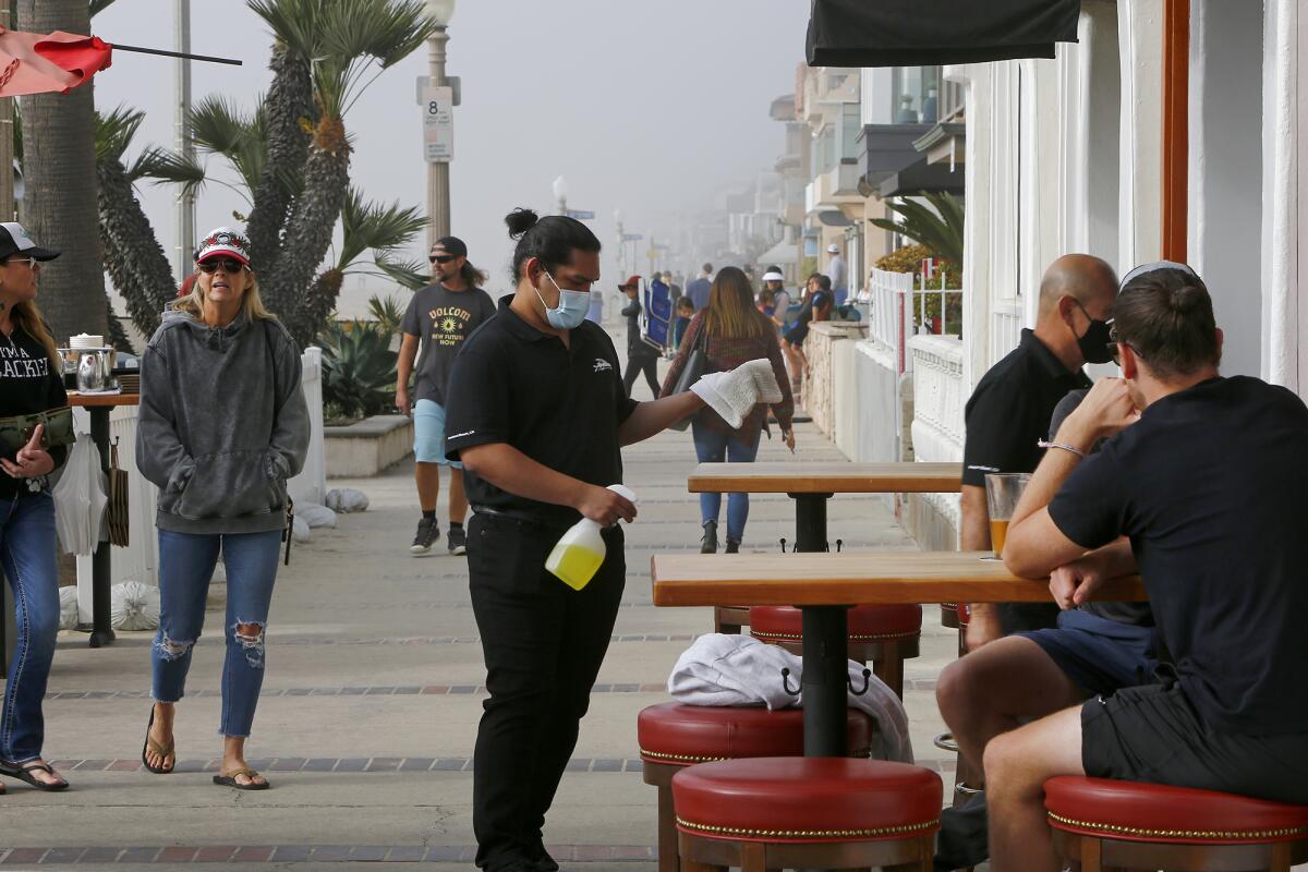 A server sanitizes a table and stools before seating customers at Newport Beach Hotel's outdoor dining area on Tuesday.