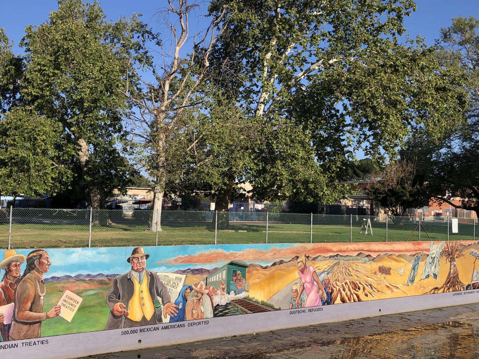 Mural panels in a concrete arroyo show Indigenous men and a man representing a 1930s politician, among other figures