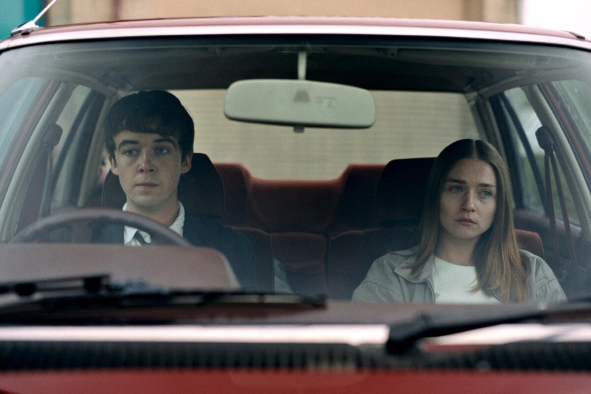 A young man and a young woman sit in the front seat of a car.