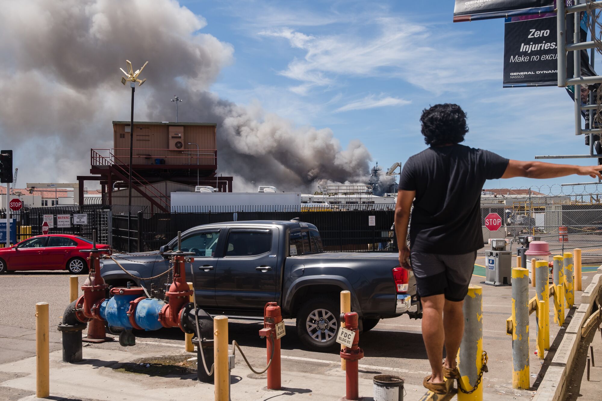 A person watches the USS Bonhomme Richard on fire from outside the naval base.