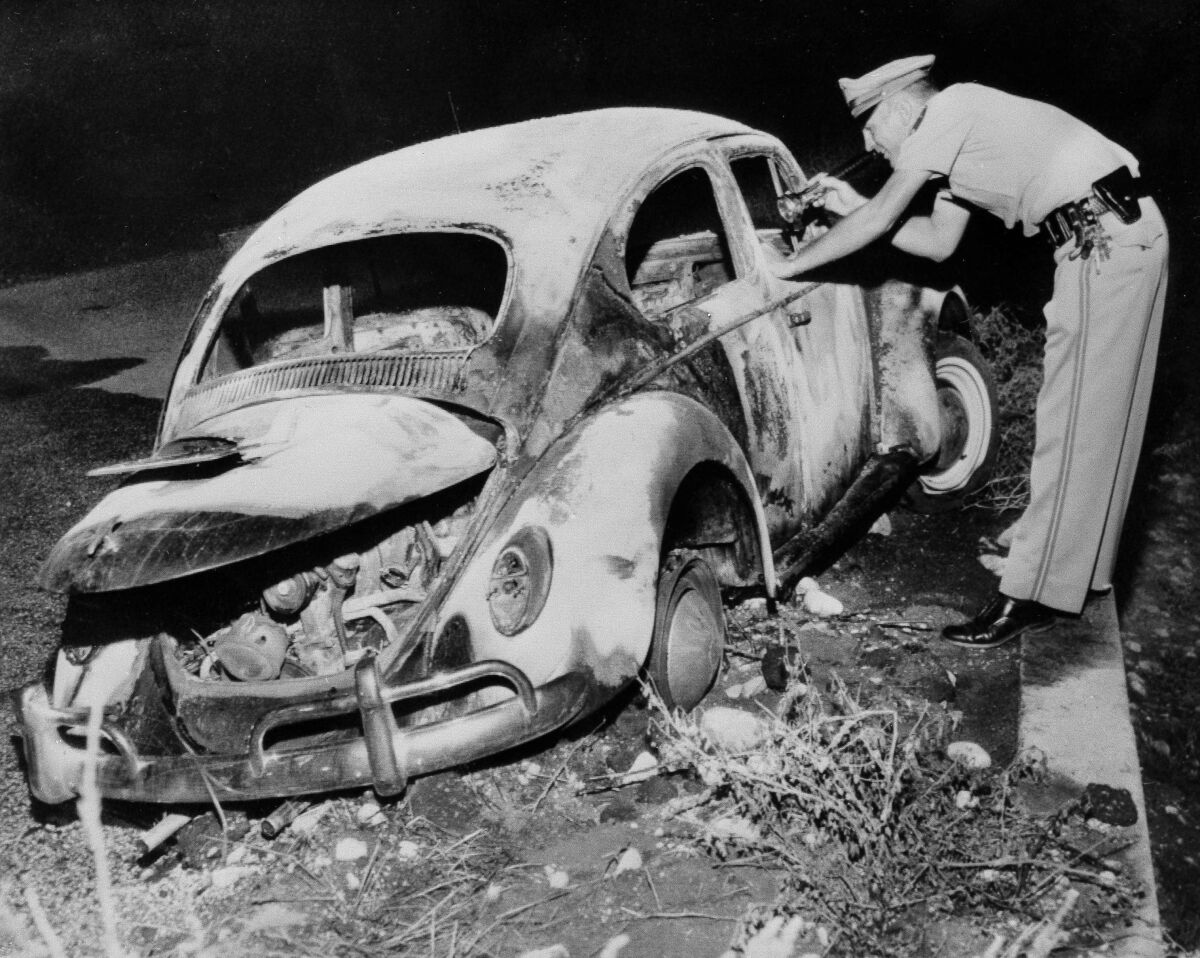 A police officer looks at the charred Volkswagen Beetle in which Gordon E. Miller was found dead, in San Bernardino.