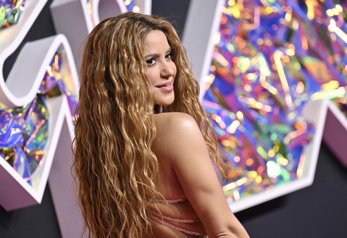 Shakira in a sleeveless nude-colored gown smiling and looking over her shoulder at the MTV VMAs red carpet