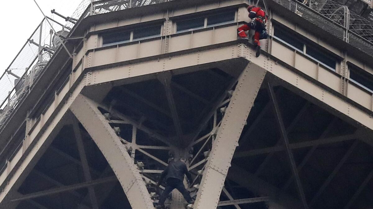 A rescue worker, top in red, hangs from the Eiffel Tower while a climber stands below him between two iron columns on May 20, 2019.