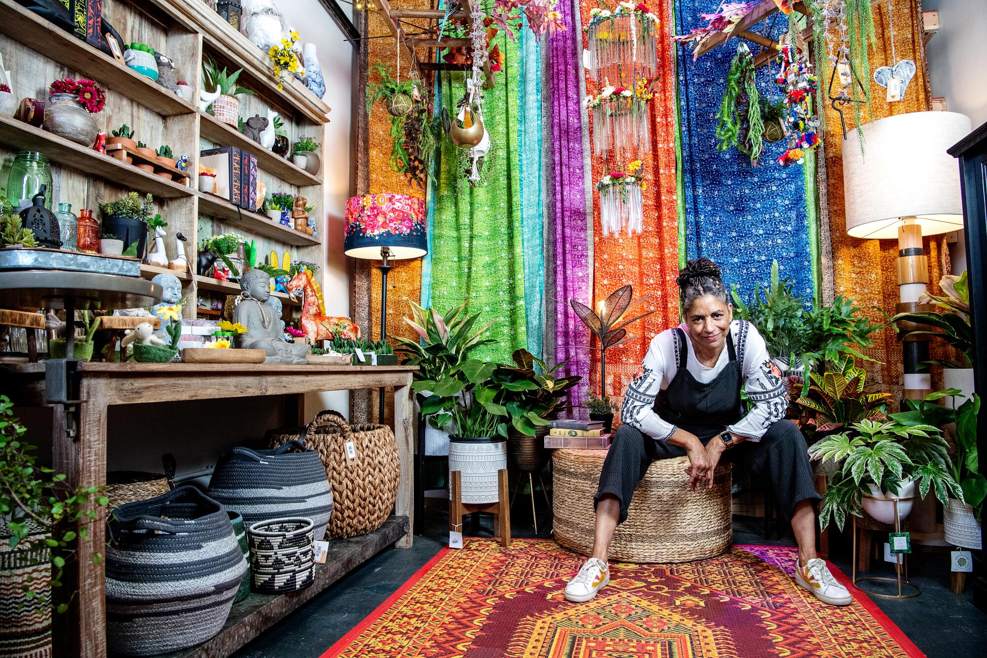 A seated woman surrounded by colorful plants and fabrics.