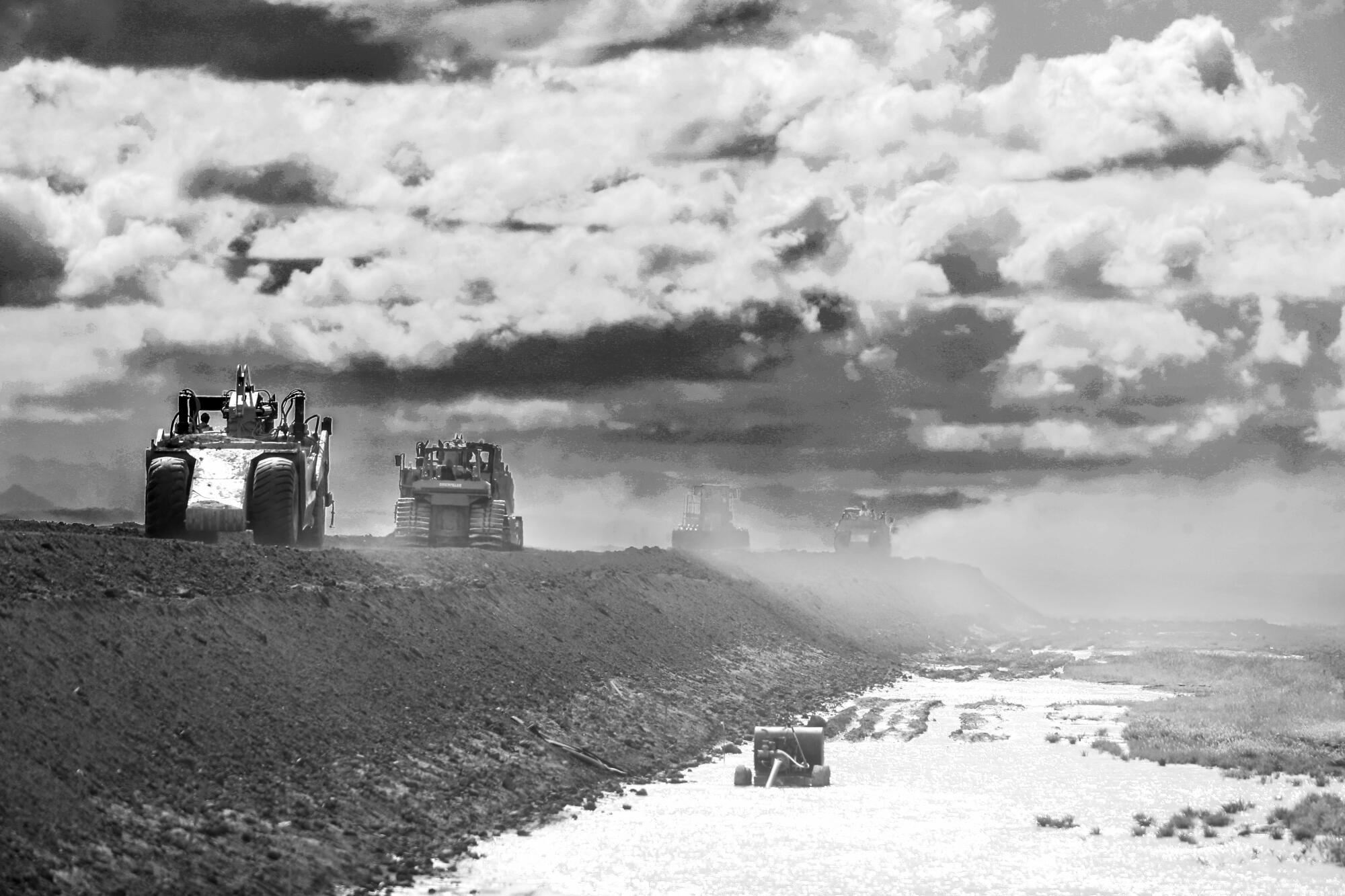 Earth movers parade along a levee near the Tule River.