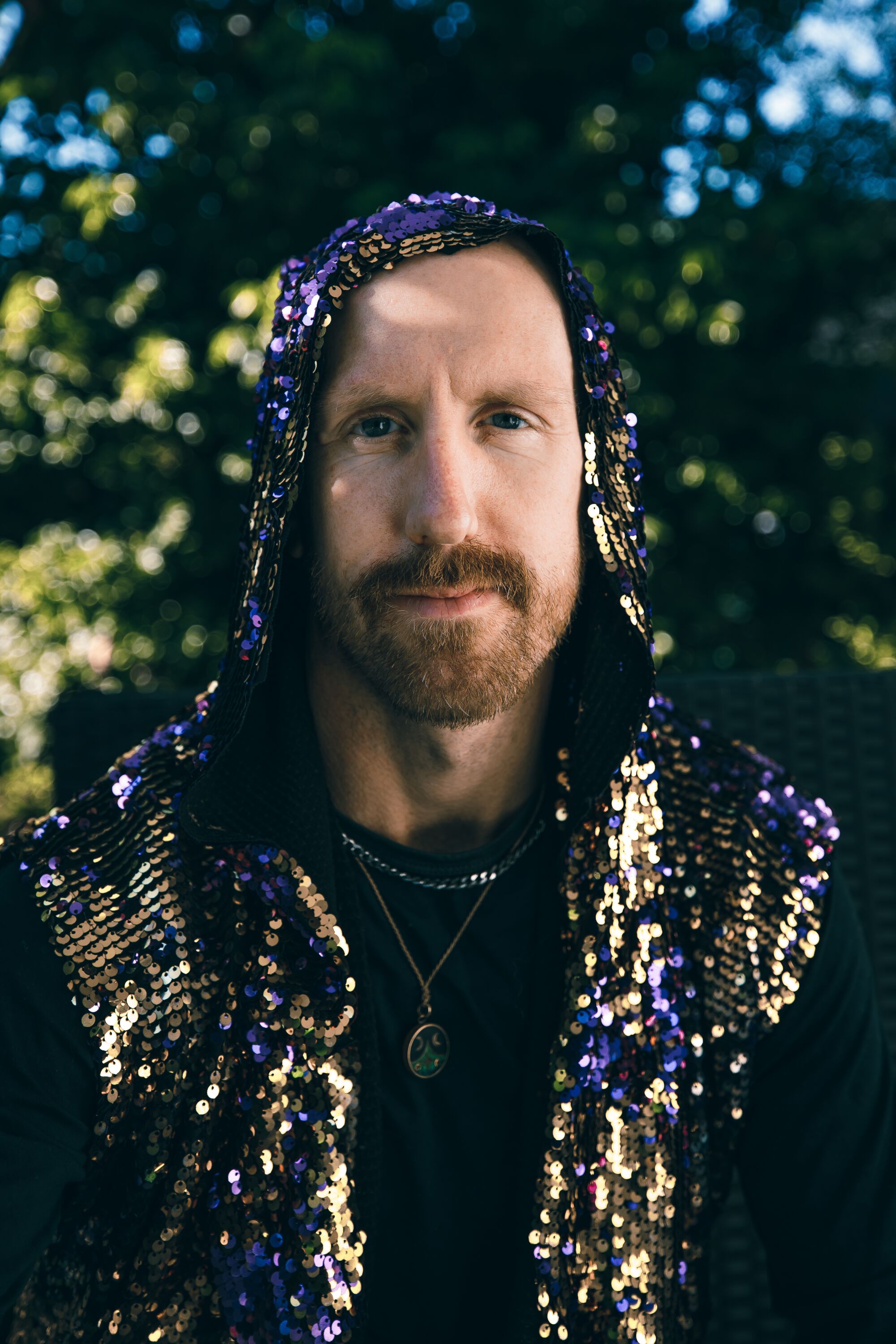 A man with a goatee and mustache, wearing a glittery hoodie.