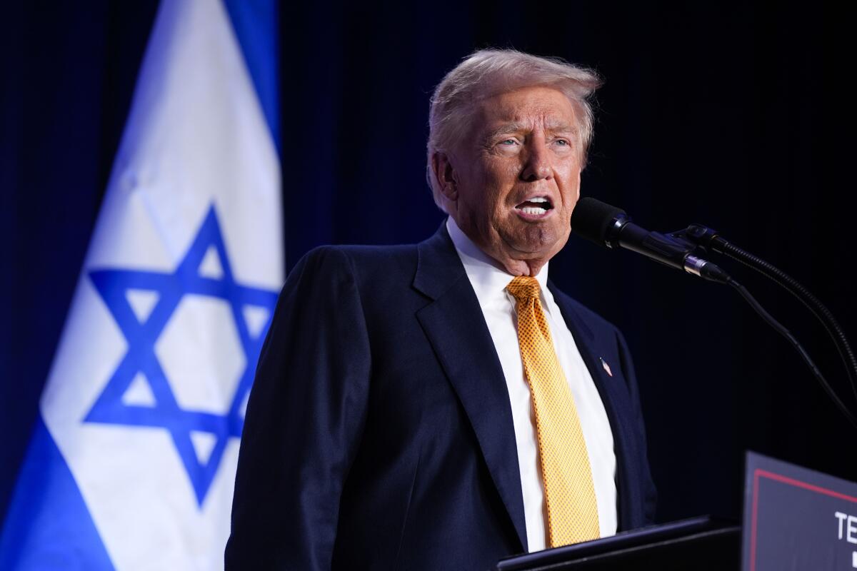 Donald Trump speaks into a microphone with an Israeli flag in the background