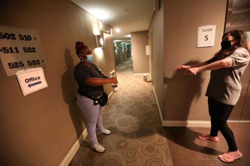 LOS ANGELES, CA - JULY 21, 2020 - - Guest services associate Mia Rogers, 23, left, listens to Fire Wilson, 66, remember to social distance while they conversed at a Project Roomkey hotel in Los Angeles on July 22, 2020. Wilson is a Project Roomkey guest at the hotel. Rogers, a client of Chrysalis, lost her job due to the coronavirus pandemic. She was hired to work at a Project Roomkey hotel. About 100 clients of Chrysalis, a downtown agency that gets work for homeless people who lost their jobs because of the virus shutdowns. They've been rehired by Project Roomkey to work in hotels. (Genaro Molina / Los Angeles Times)