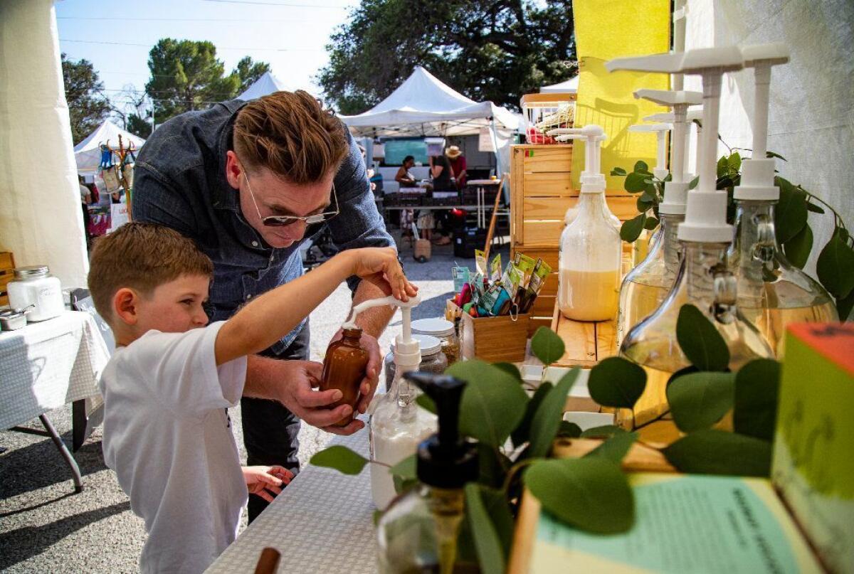 Jasper Watts ayuda a su hijo James, de 5 años, a poner el champú en un recipiente de vidrio en la estación de recarga de Sustain L.A en Altadena Farmers Market.