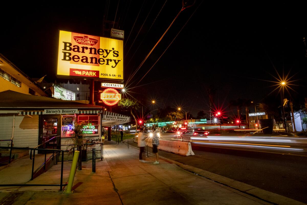 The exterior of a bar at night with a brightly lit sign that reads Barney's Beanery.